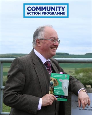 Commissioner in front of field gate holding a leaflet